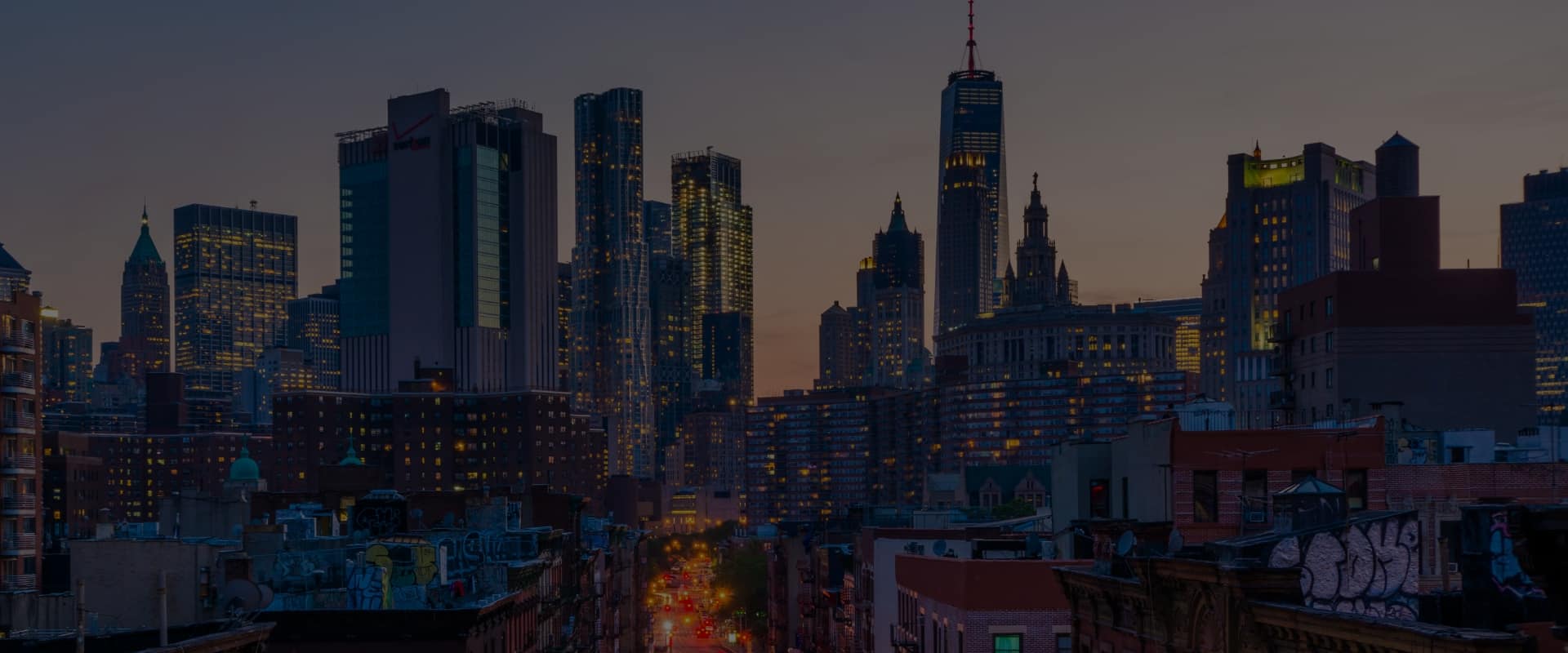Twilight over a dense urban skyline with illuminated buildings.