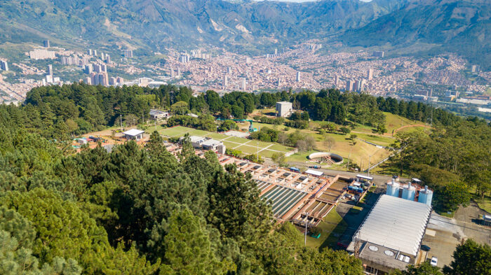 Aerial view of a water treatment facility in Medellín, Colombia, surrounded by trees, with a city and mountains in the background—providing reliable water to the community.