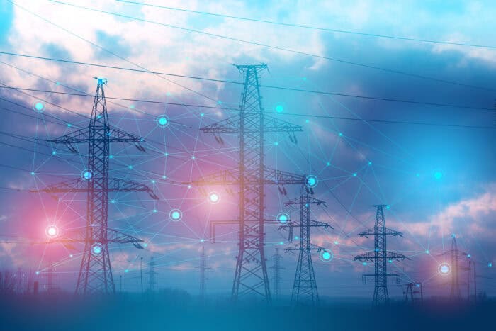 High-voltage power lines and pylons stand under a cloudy sky, overlaid with a digital network graphic representing smart grid technology.
