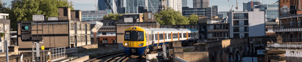 A modern yellow and blue train, a testament to engineering clarity, travels on elevated tracks through an urban area with buildings and skyscrapers in the background.