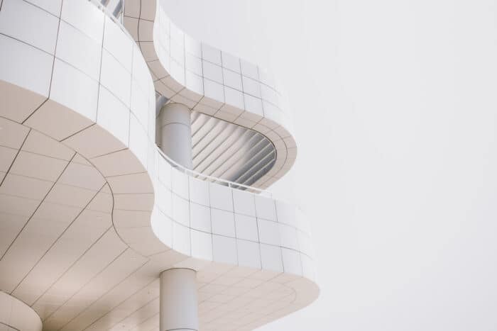 Modern architecture featuring smooth, white, curvilinear forms and vertically aligned windows, with structural columns supporting multiple levels. The design emphasizes clean lines and minimalism.