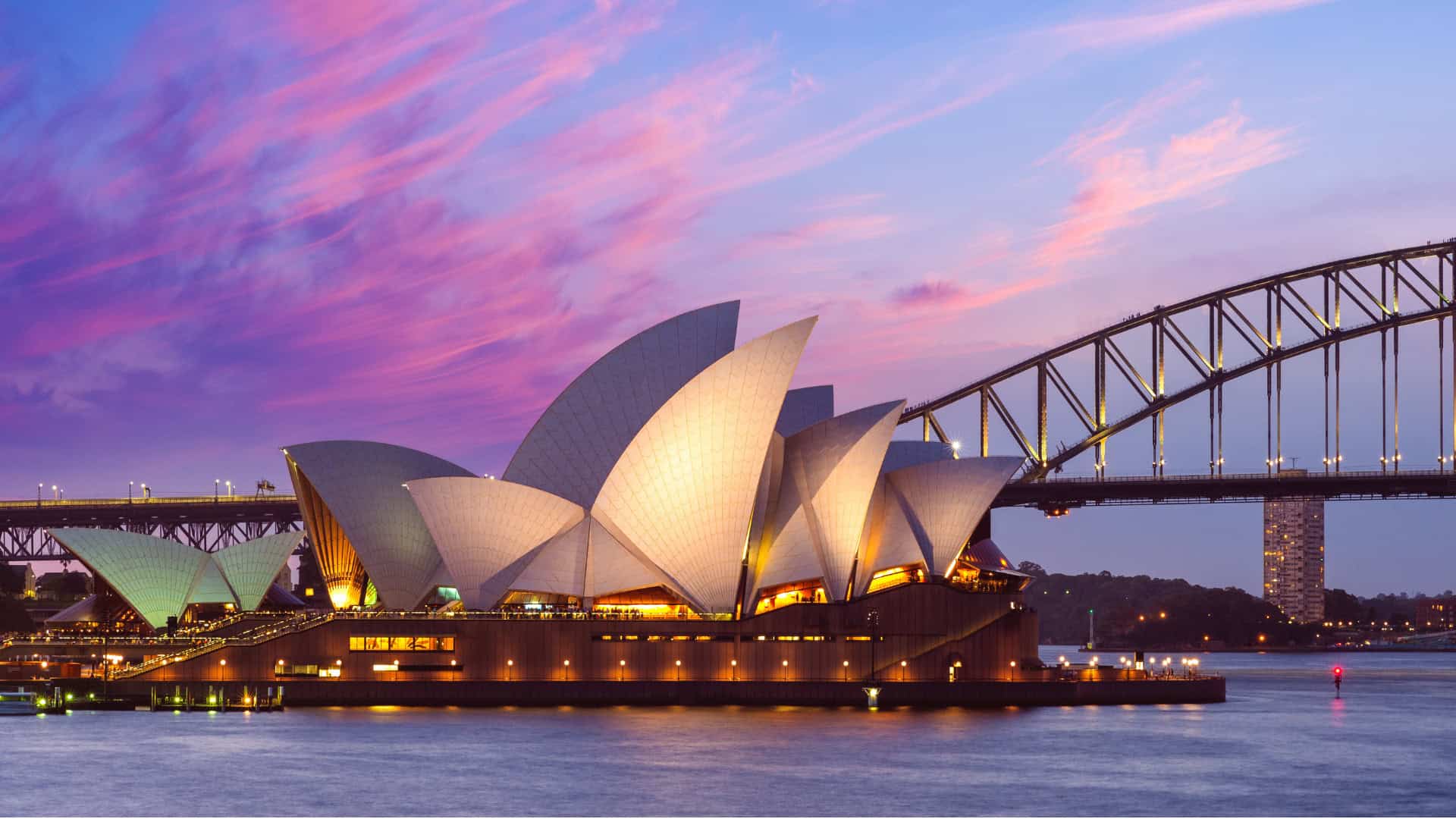 Sydney Opera House and Harbour Bridge at dusk with a colorful sky, viewed from across the water—an iconic example of how infrastructure can inspire reinvention and connect a city through architecture.