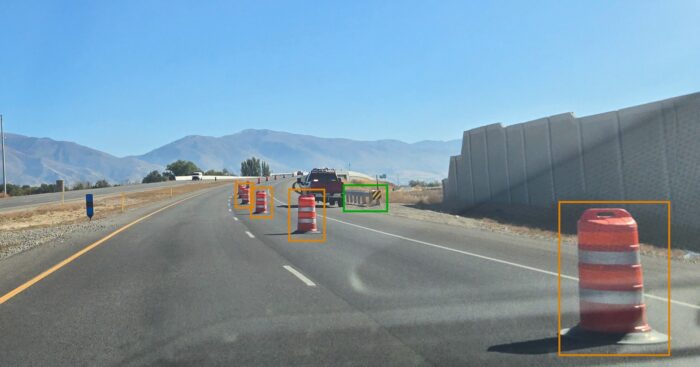 A road with traffic barrels and a truck in the distance.