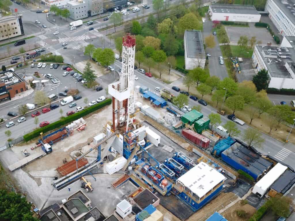 Aerial view of a construction site with drilling equipment for geothermal heat, surrounded by trees and buildings near a busy Paris intersection, paving the way for a low carbon future.