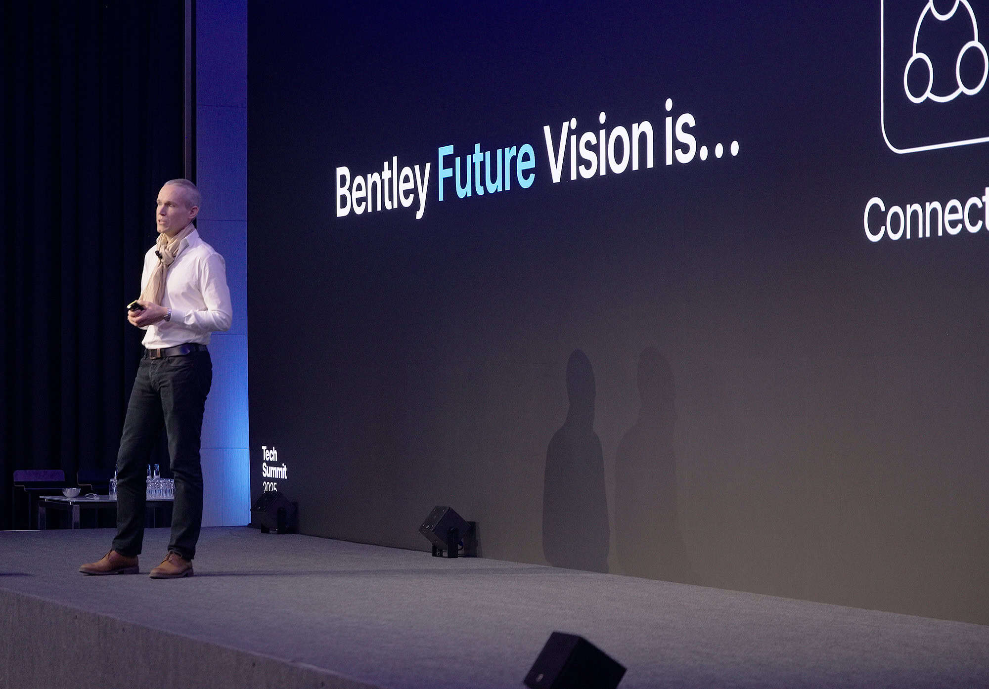 A man stands on stage presenting next to a screen displaying the text "Bentley Future Vision is..." and an icon labeled "Connect.