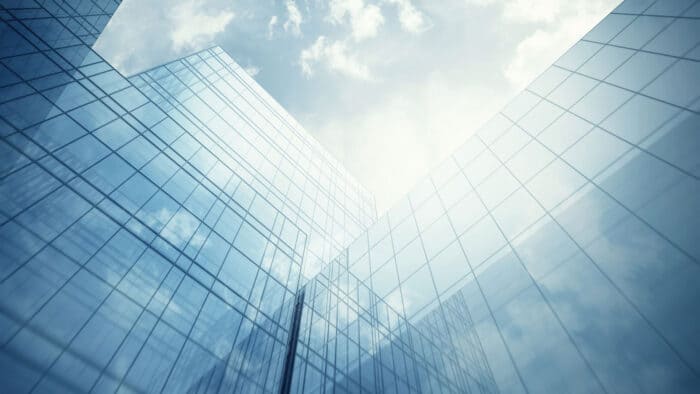 Low-angle view of modern glass skyscrapers reflecting the cloudy sky.