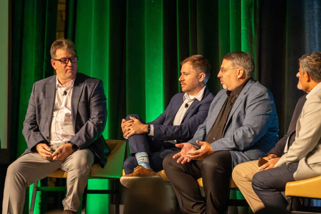 Four men in suits sit on a panel stage, discussing engineering insights in front of a green curtain backdrop at the 2025 Bentley Civil User Conference.