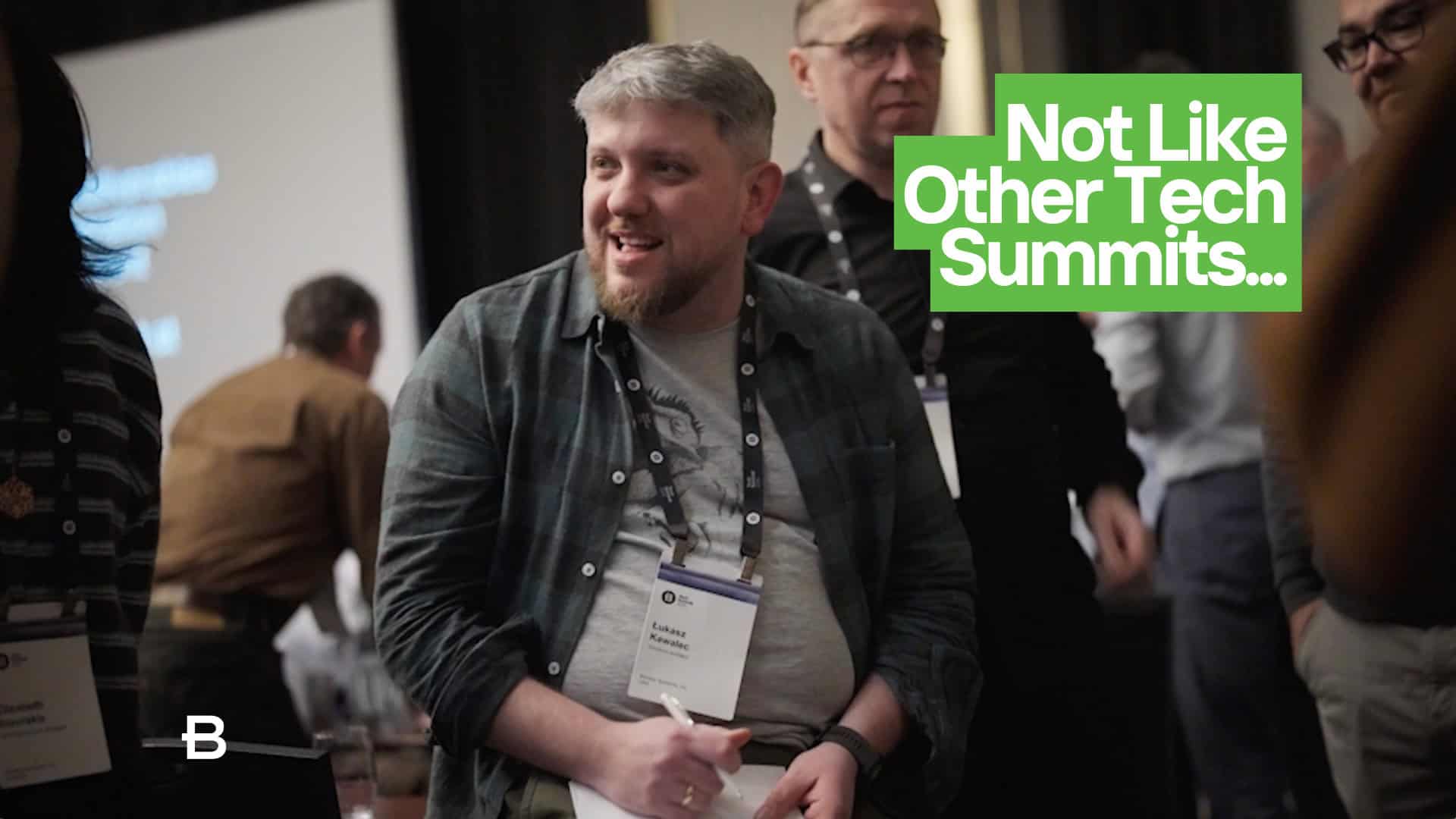 A man wearing a name tag sits and smiles among a group of people at an event in Berlin. Text on screen reads "Not Like Other Tech Summits...," highlighting Bentley Teams tackling infrastructure challenges together.