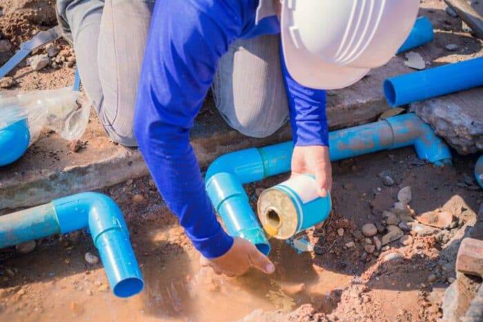 construction worker working on a blue pipe in the ground