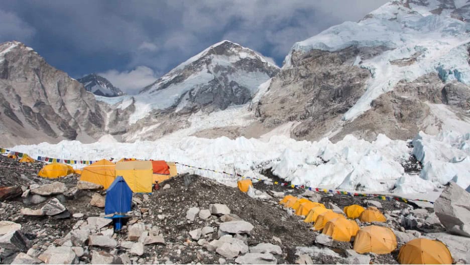 Rows of yellow tents are set up on rocky ground at a high-altitude mountain base camp, with snow-covered peaks in the background—much like streamlined engineering workflows navigating challenging environments under a cloudy sky.