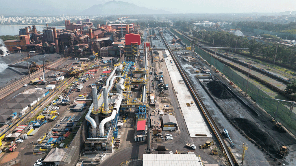 Aerial view of an industrial complex with large machinery, factories, and construction work alongside rail tracks and storage areas.