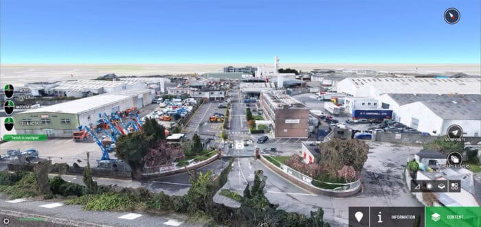 A digital street view of an industrial complex with warehouses, parked vehicles, and various outdoor equipment under a clear blue sky.