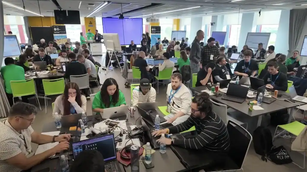 A large group of people work on laptops and collaborate in a busy, modern conference room with bright lighting and open seating—perfect for capturing content for your Homepage Video Playlist.