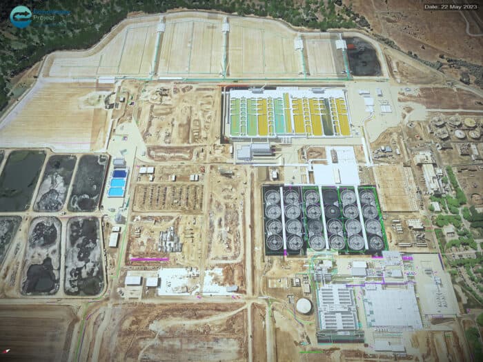 Aerial view of a construction site featuring multiple buildings, storage tanks, industrial equipment, and infrastructure development. Date: 22 May 2023, seen on the top right of the image.