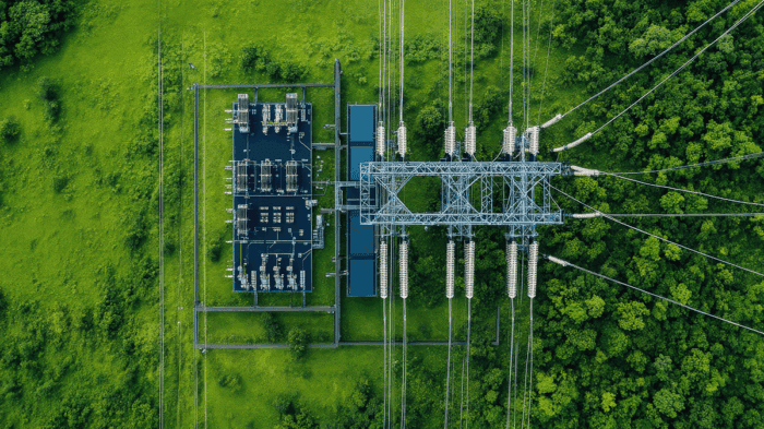 Aerial view of an electrical substation with power lines, highlighting the role of electric utilities in balancing sustainability near a forested area and grassy field.