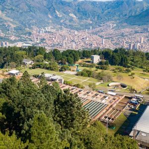 Empresas PĆŗblicas de MedellĆn (EPM) Aerial view of a water treatment facility in MedellĆn, Colombia, surrounded by trees, with a city and mountains in the backgroundāproviding reliable water to the community.
