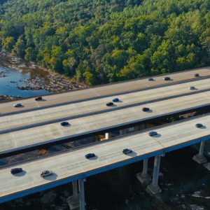Aerial view of two parallel highways with cars driving, surrounded by trees and a river below.