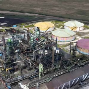 Aerial view of an industrial facility featuring large circular storage tanks and metal infrastructure, surrounded by open land, captured in crisp detail reminiscent of Gaussian splats.