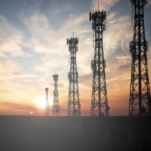 Five communication towers stand silhouetted against a sunset sky with scattered clouds.