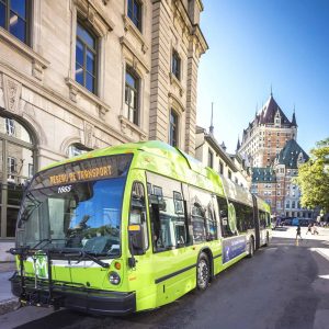 A green city bus labeled "Réseau de Transport," part of Québec City Transportation Planning, is parked on a sunny street with historic buildings and Château Frontenac in the background.