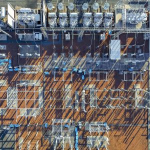 Aerial view of an electrical substation showing transformers, power lines, and metal frameworks casting long shadows—highlighting the vital role substations play in supporting the wind energy future from ambition to execution.