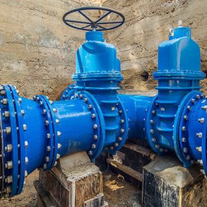 Two large blue industrial water valves are connected to black pipes within a concrete enclosure, highlighting the importance of water system optimization in modern infrastructure.
