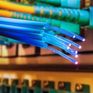 Close-up of illuminated blue fiber optic cables with connected components in the background.