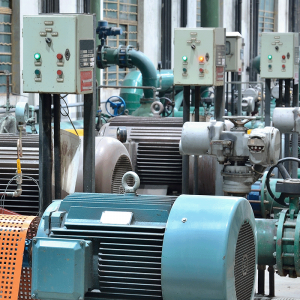 Row of industrial pumps and motors with green pipes and control panels in a factory setting, showcasing resilient water infrastructure designed for efficiency and reduced energy costs.