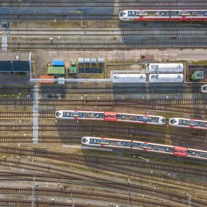Aerial view of a train yard with multiple trains parked on parallel tracks, adjacent buildings, and various service equipment visible.