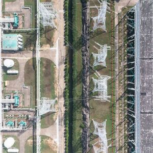 Aerial view of an industrial facility with machinery, tanks, and electrical grid structures divided by pathways and green areas.