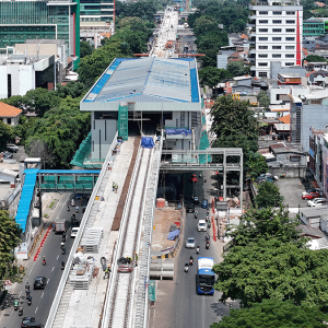 Aerial view of an elevated train station under construction in a dense urban area, with surrounding buildings and cars on the road below.