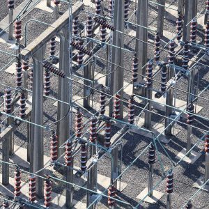 Aerial view of an electrical substation showcasing efficient substation design with numerous insulators, metal supports, wires, and a gravel ground surface.
