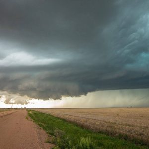 A large, dark storm cloud looms over a rural dirt road and open fields, with rain visible in the distance—evoking the visualization challenges faced before innovative solutions like iTwin Engage.
