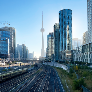 Downtown Toronto cityscape with train tracks and advanced rail protection in the foreground, modern high-rise buildings, and the CN Tower visible in the center background under a clear sky—showcasing Toronto rail safety innovators at work.