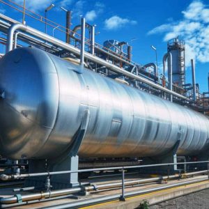 Large industrial metal pressure vessel designed for optimal stress analysis, with interconnected pipes and platforms at a processing facility under a partly cloudy blue sky.