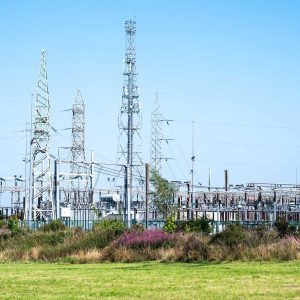 Electric power substation with multiple metal frameworks, transmission towers, and electrical equipment under a clear blue sky, surrounded by grass—ideal for analyzing or mapping a substation data model.