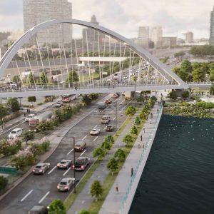 A wide bridge with arch supports, part of a YII Project, spans over busy multi-lane roads beside a waterfront, with city buildings and greenery in the background.