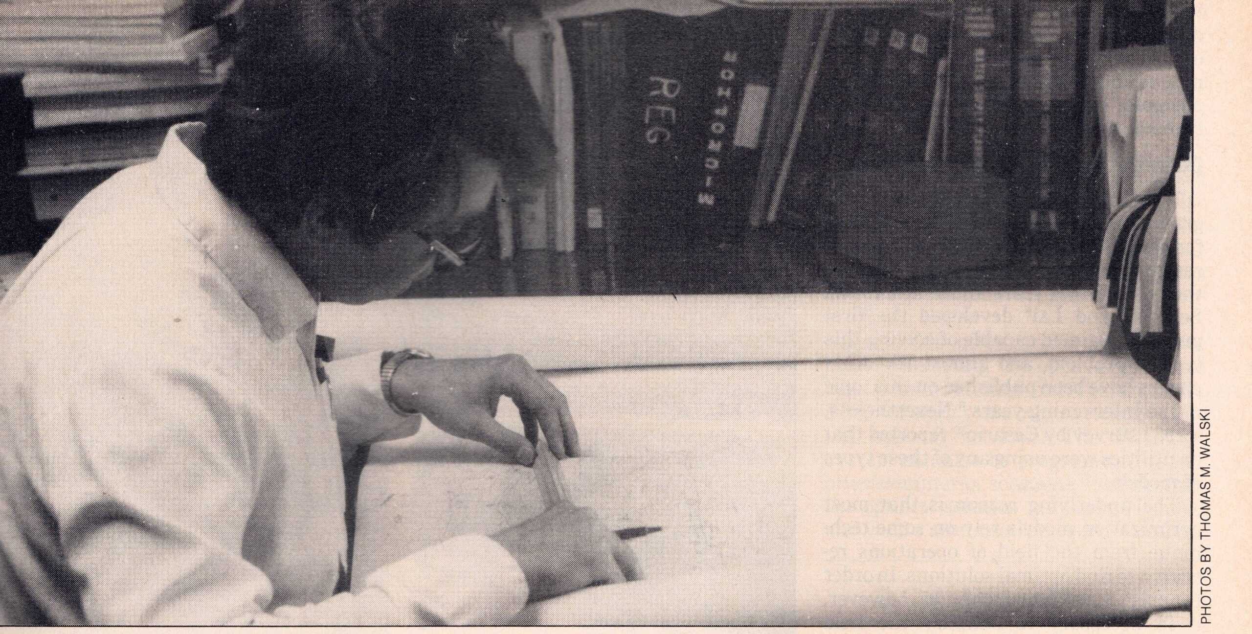 A person reviews large sheets at a desk surrounded by organized books, files, and engineering graphs.