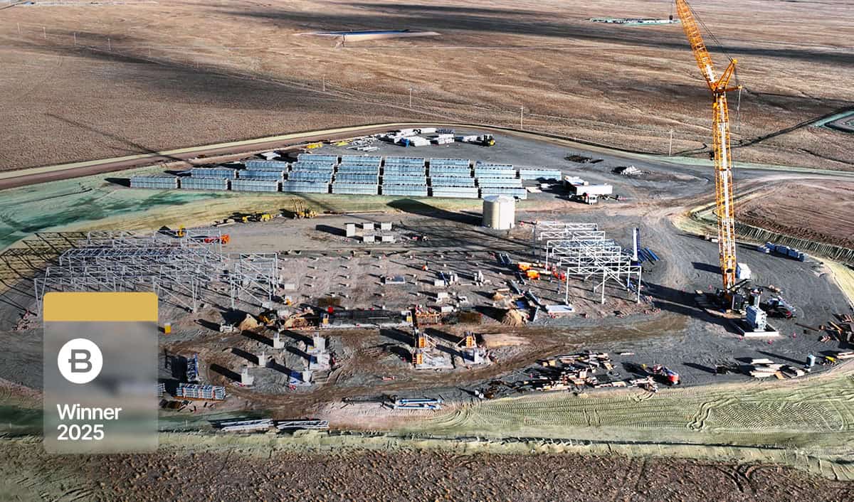 A large construction site with steel framework, heavy machinery, stacked materials, and a tall yellow crane in a flat landscape, showcasing the YII Project. A "B Winner 2025" badge is overlaid on this Project Profile image.