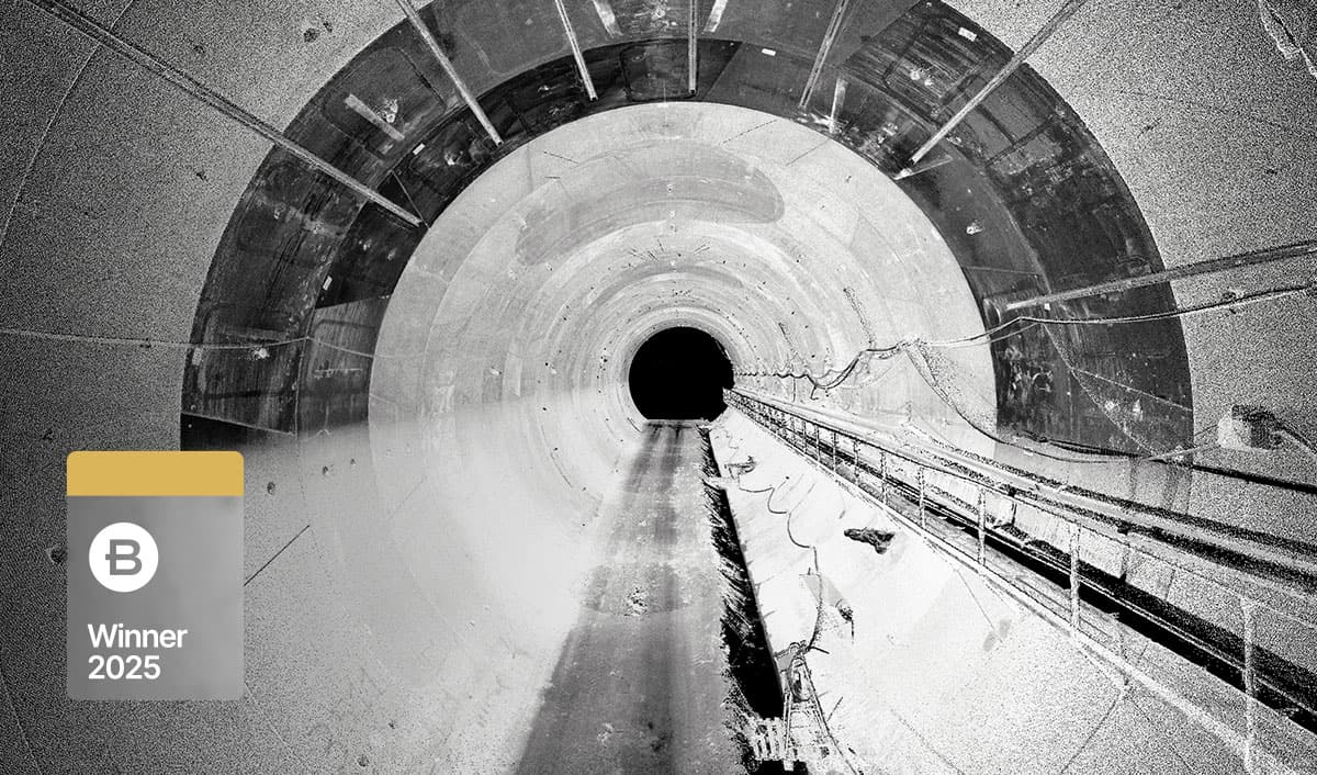 Black and white image showing the interior of a large, circular tunnel with cables running along the right side—an impressive project by Italferr S.p.A.; a gray badge at left reads “B Winner 2025.”.