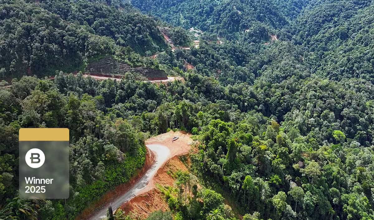 A winding dirt road cuts through dense, green forested hills in East Malaysia, with a “YII Winner 2025” badge overlaid in the lower left corner of the image.