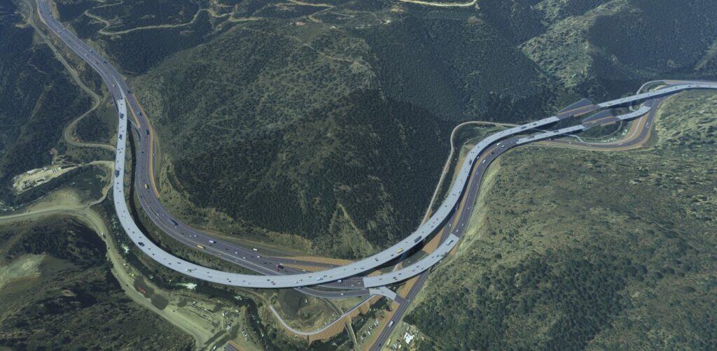 Aerial view of a large highway interchange with multiple overpasses and cars, surrounded by hilly, forested terrain—an impressive example of how engineering firms drive digital transformation in modern infrastructure.
