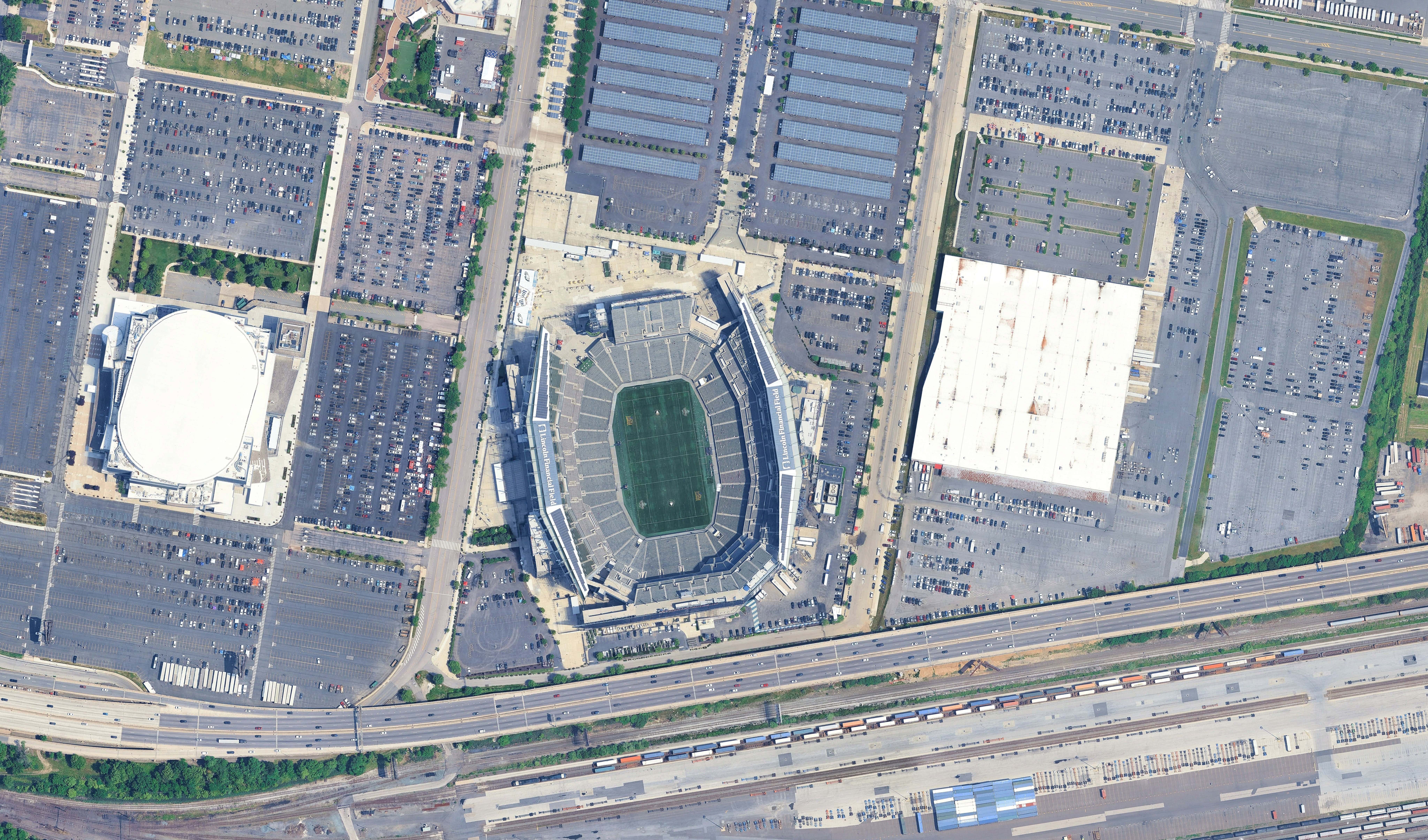 Aerial view of a large stadium with a green field, surrounded by parking lots, roads designed with OpenRoads Designer 2026, and nearby buildings—capturing the vibrant atmosphere of a summer of football.