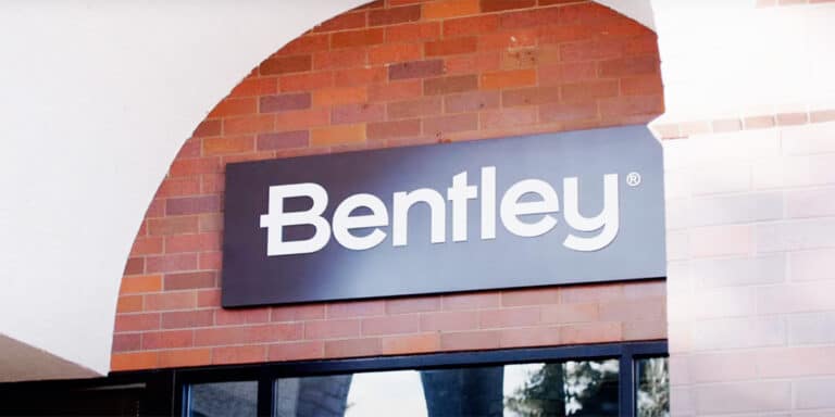 A rectangular sign with the word "Bentley" in white letters is mounted on a brick wall above a glass window, highlighting Bentley’s innovation in AI in civil engineering.