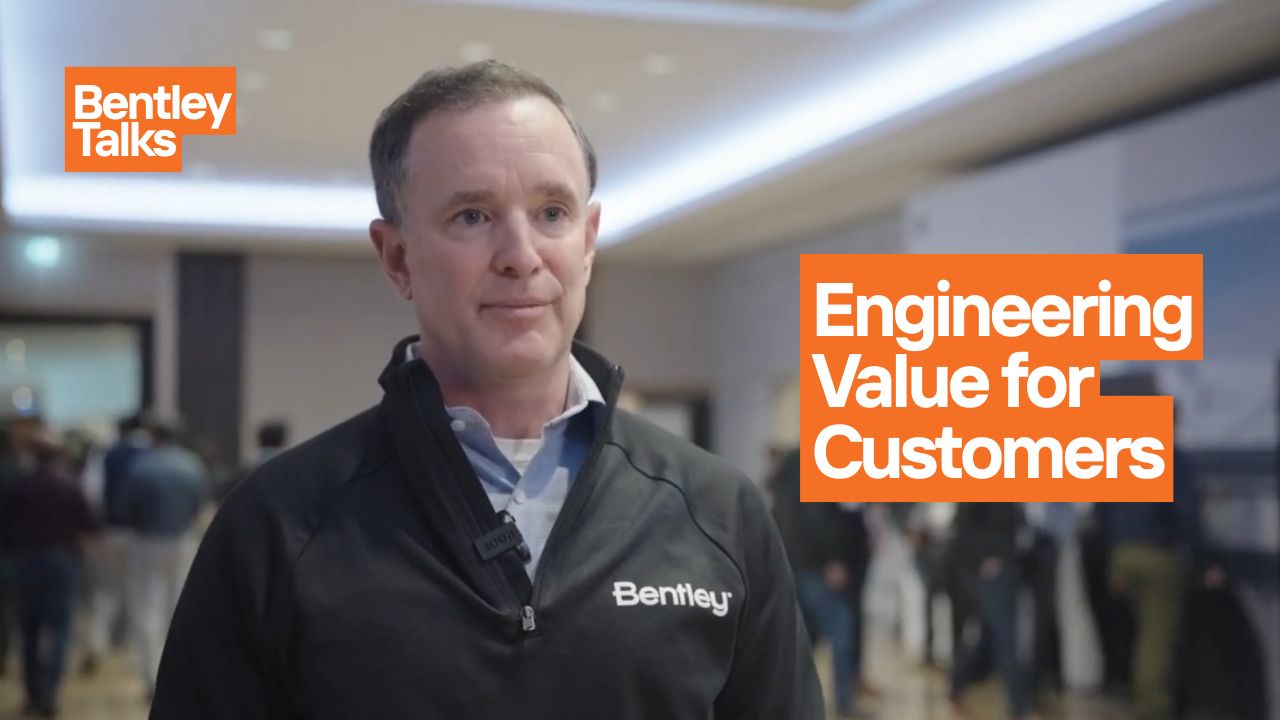 A man in a Bentley-branded jacket speaks at an event focused on business value; the text reads "Engineering Customer Pain Points" and "Bentley Talks," with several people blurred in the background.
