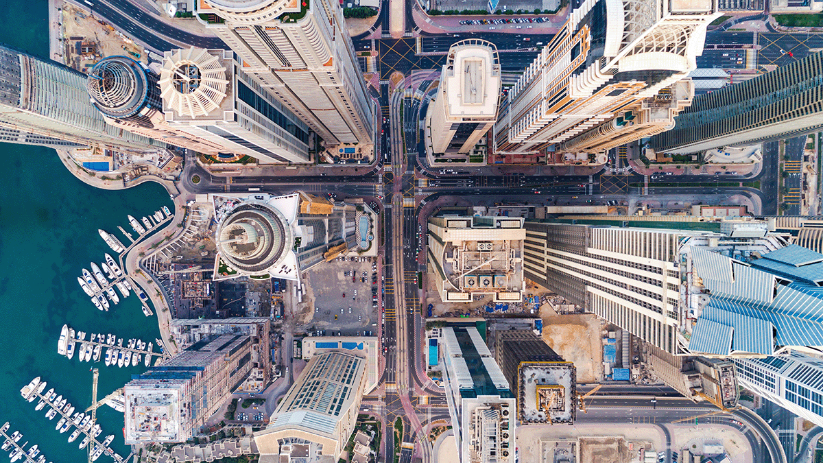 Aerial view of a city intersection with tall skyscrapers, busy roads, and a marina with boats