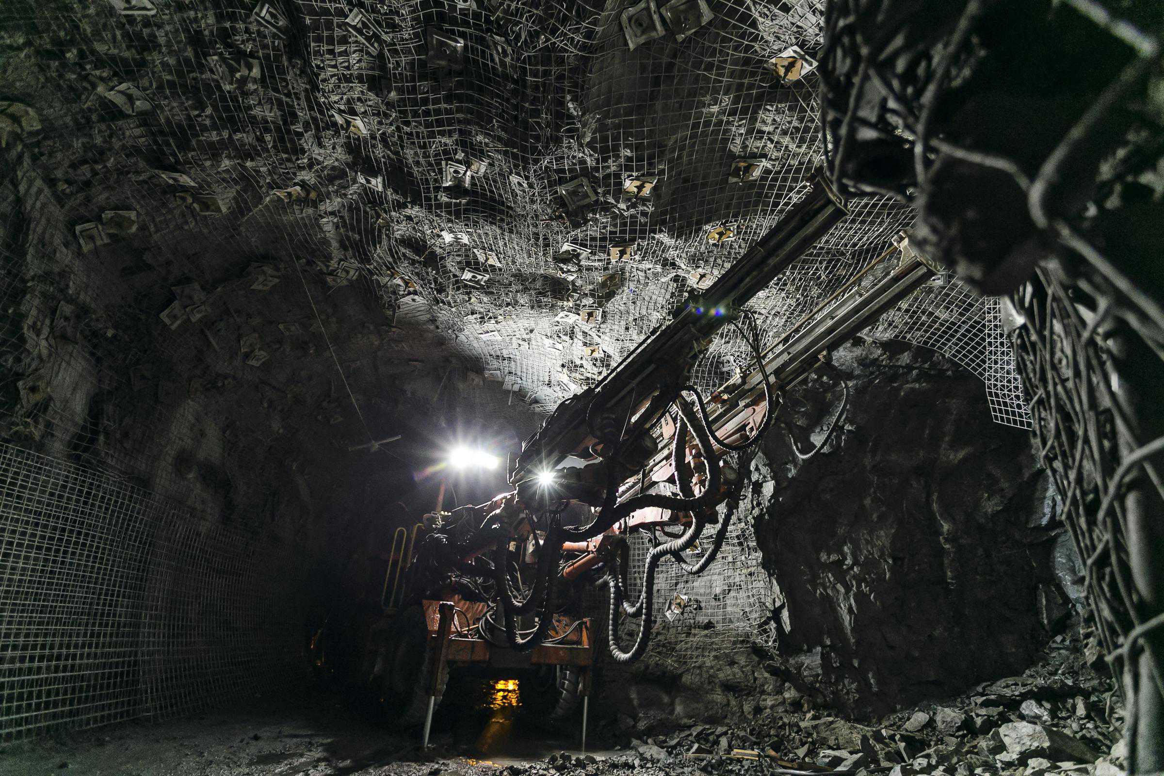 An underground mining machine operates in a dimly lit tunnel, with rock walls reinforced by wire mesh, leveraging advanced methods from the Tunnelling Library.