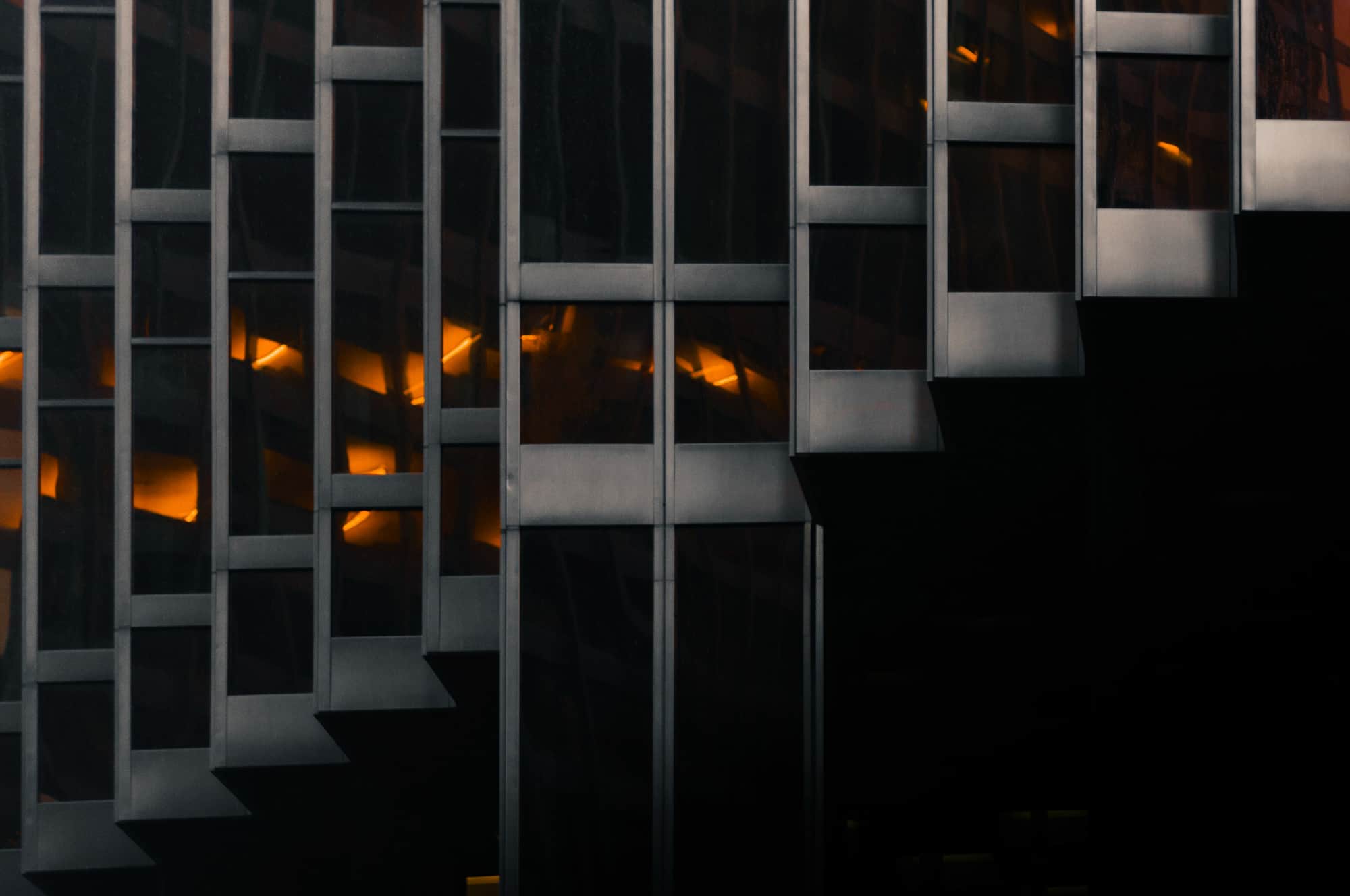 Abstract view of a modern building with geometric patterns and warm lights visible from within.