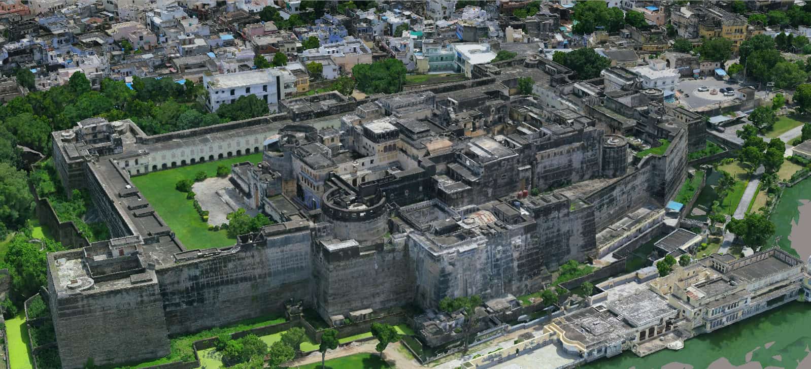 Aerial view of a large historic stone fort in India, surrounded by green lawns, dense city buildings, and a nearby river—an ideal scene for City Digital Twin Mapping powered by MapmyIndia.