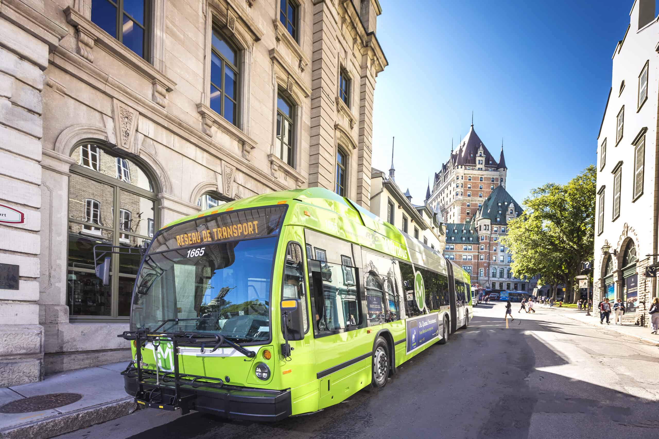A green city bus labeled "Réseau de Transport," part of Québec City Transportation Planning, is parked on a sunny street with historic buildings and Château Frontenac in the background.